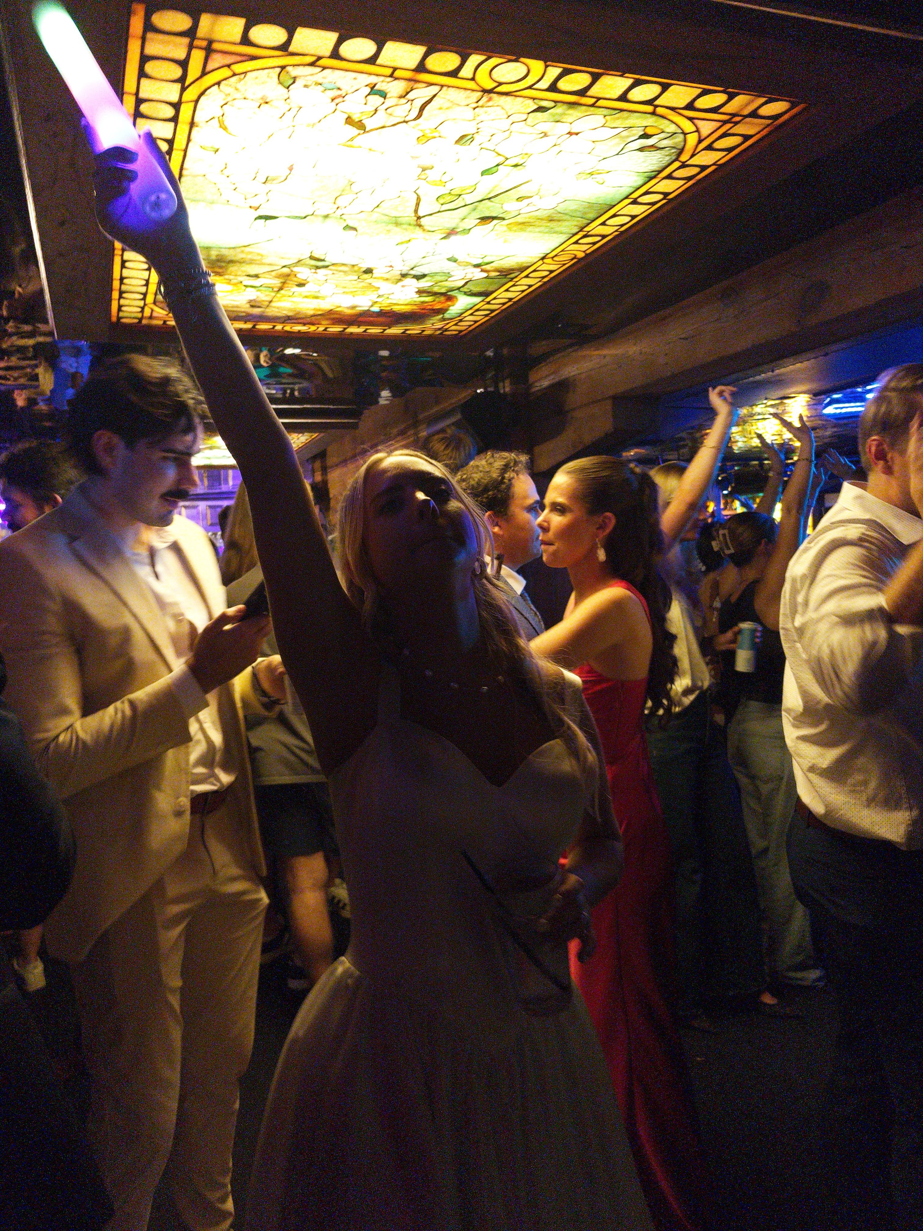 Bride on the dance floor holding a purple LED stick under a stained-glass ceiling panel