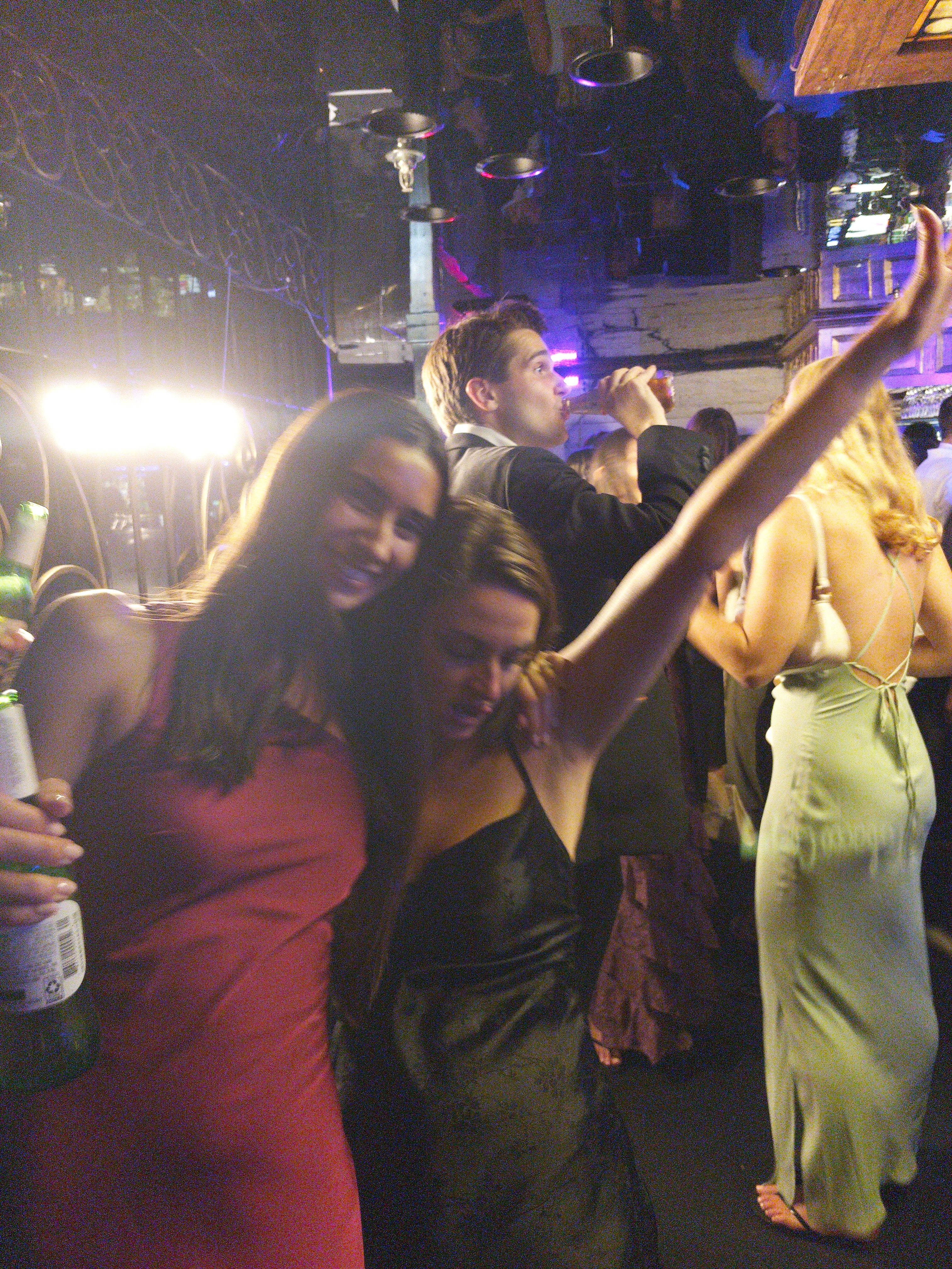 Afterparty dance floor, magenta dress and black slip dress, beer bottle, crowded room